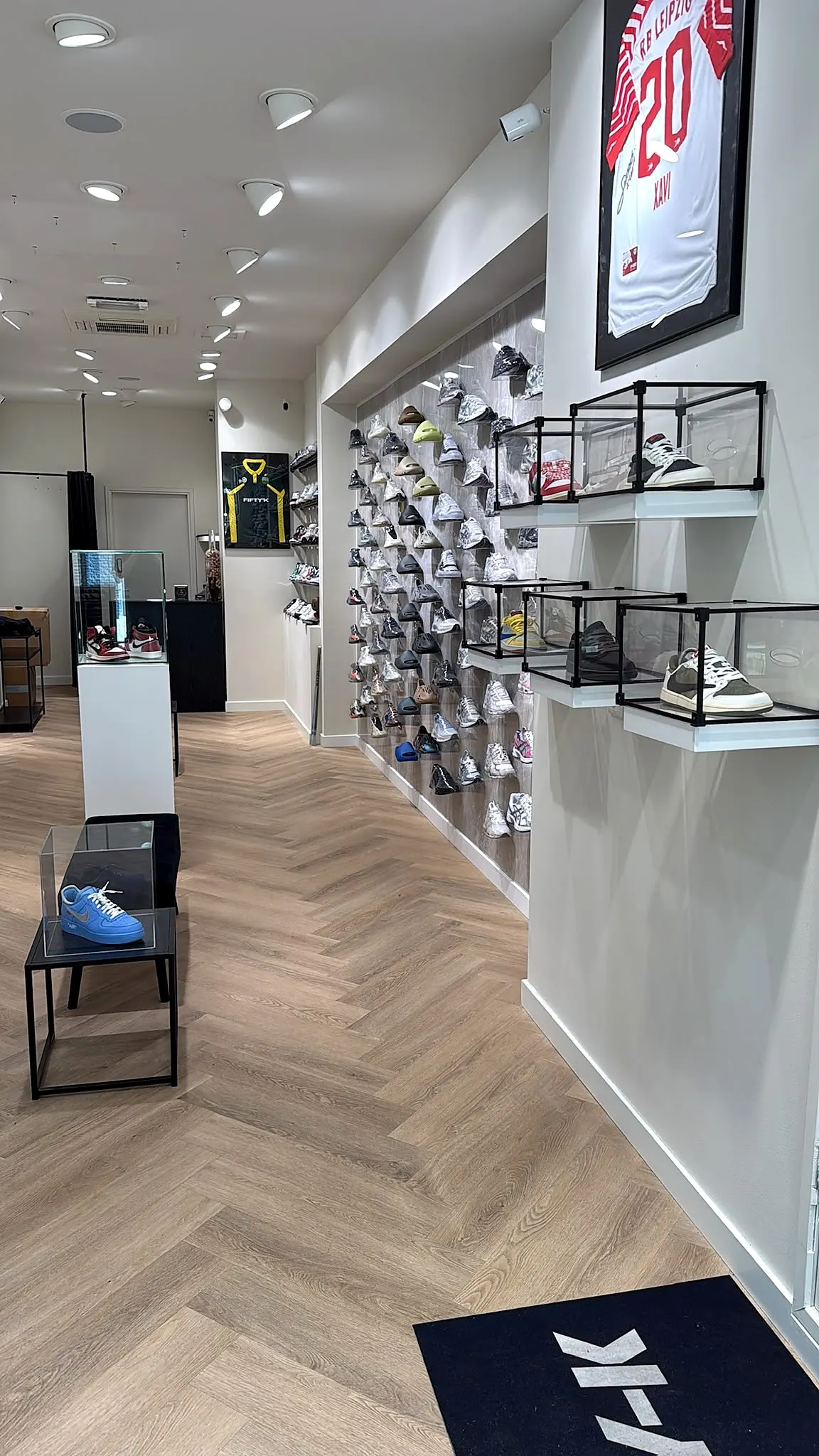 Binnen bij FIFTY-K: een lange wand vol sneakers, glazen vitrines en een visgraatvloer